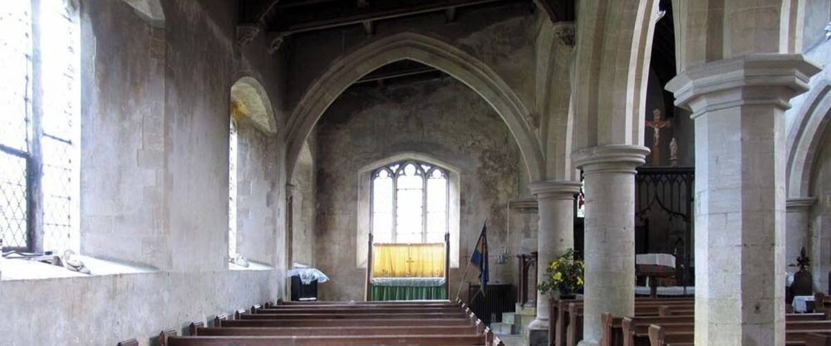 An empty church interior with wooden pews, arched ceilings, and stained glass windows.