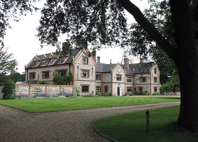 A large, historic building with a symmetrical facade, surrounded by a well-maintained lawn and a gravel path leading to the entrance.