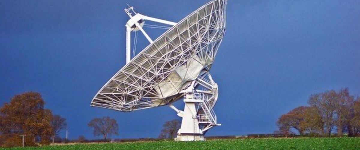 A large white radio telescope in a field with a clear blue sky.