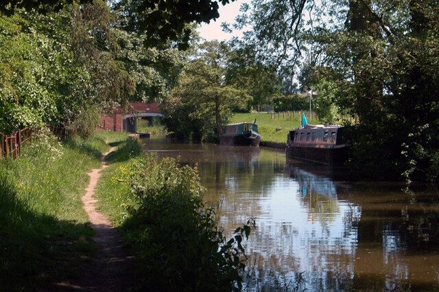 A narrow waterway with a boat docked on the right, surrounded by lush greenery and a path on the left.