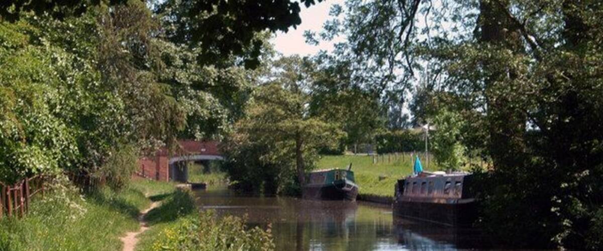 A narrow waterway with a boat docked on the right, surrounded by lush greenery and a path on the left.