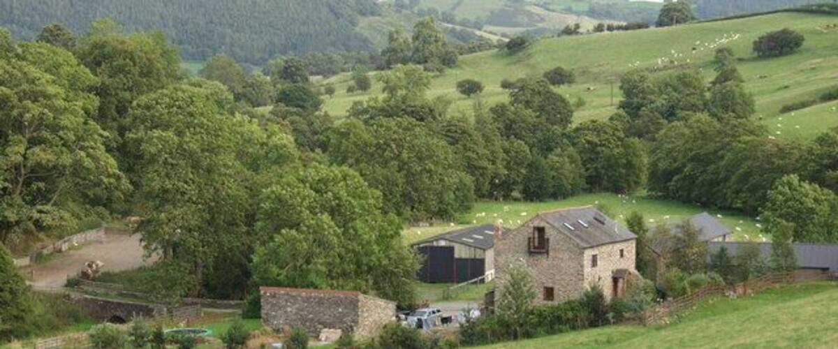 Un paisaje rural con colinas onduladas, un granero de piedra y árboles dispersos.