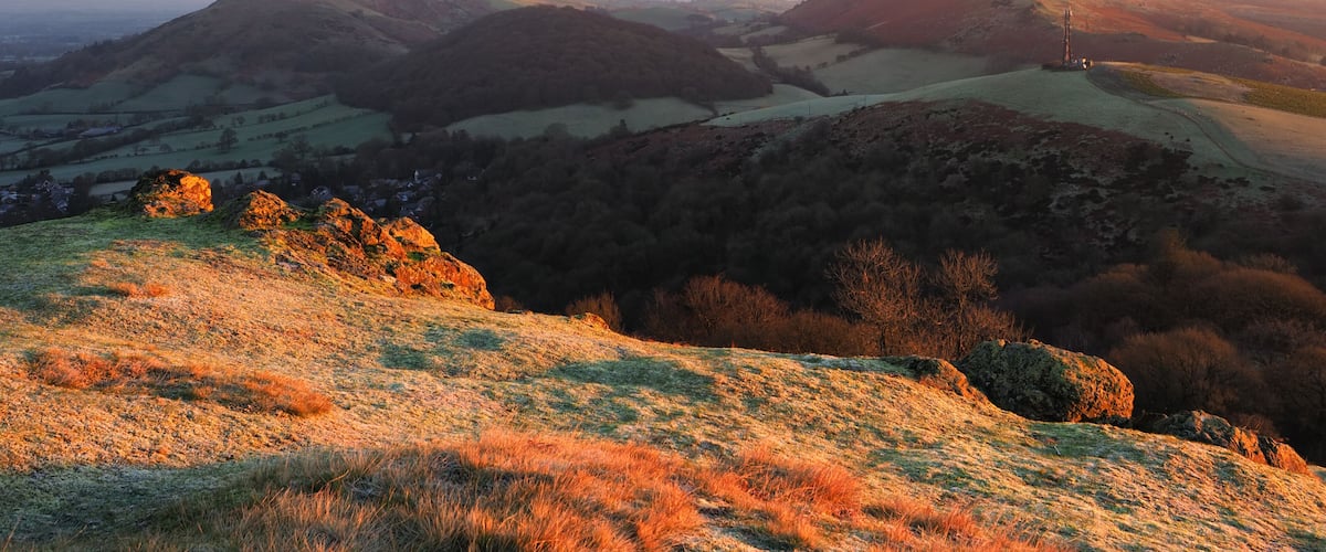 A mountainous landscape with a village in the valley, a prominent rock formation, and a distant tower.