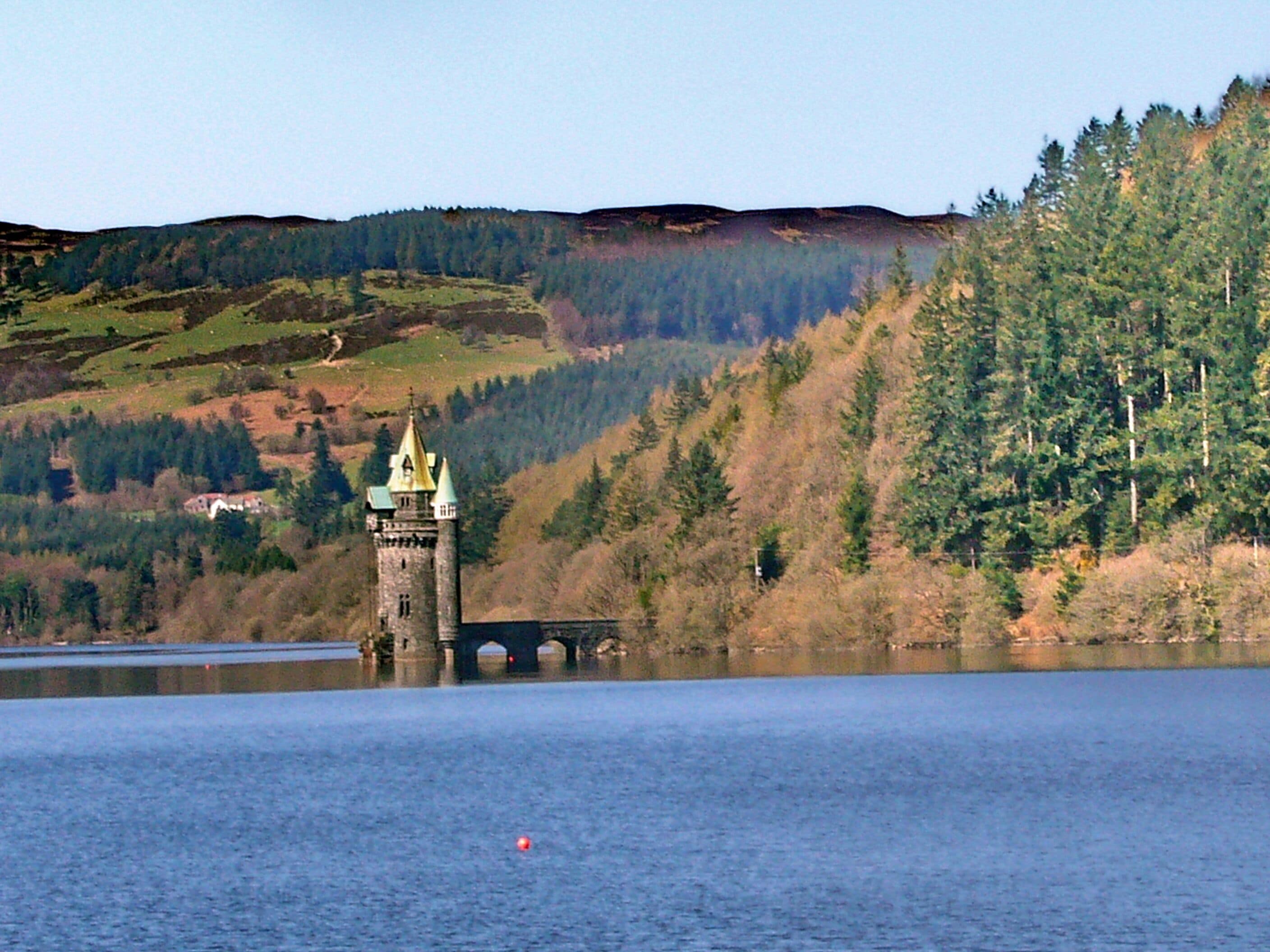 A tower with a green roof on a hill overlooking a lake.