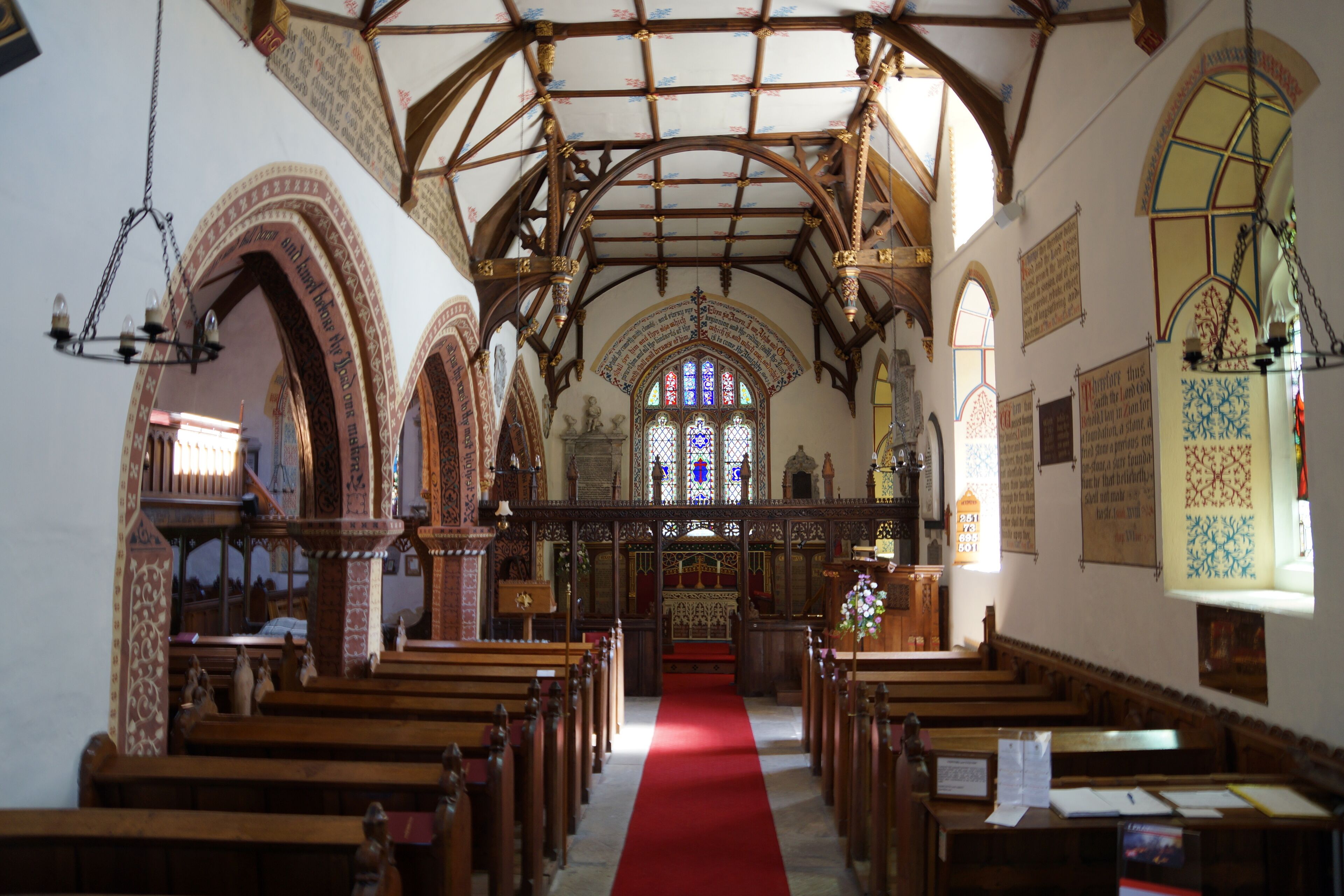 An interior of a church with wooden pews, a red carpet, stained glass windows, and Gothic architecture.