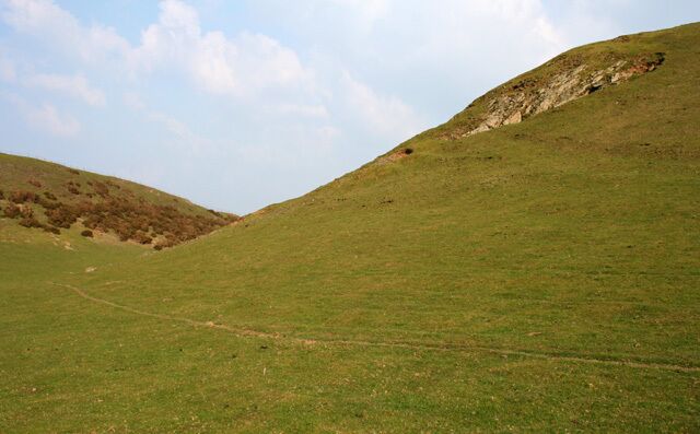 A grassy hillside with a rocky outcrop on the right and a path leading up the slope.