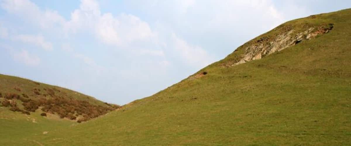 A grassy hillside with a rocky outcrop on the right and a path leading up the slope.