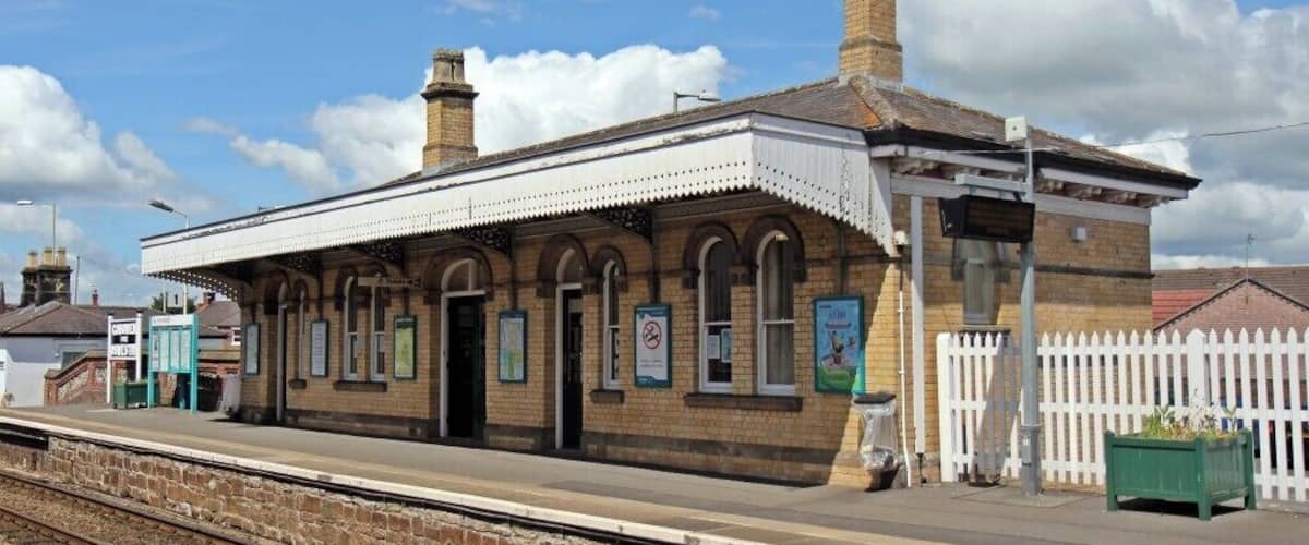 A historic train station with a brick building, arched windows, and a white picket fence.