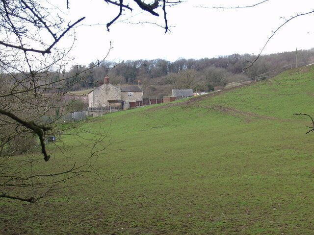 A rural landscape with a grassy hill, a stone building, and trees in the background.