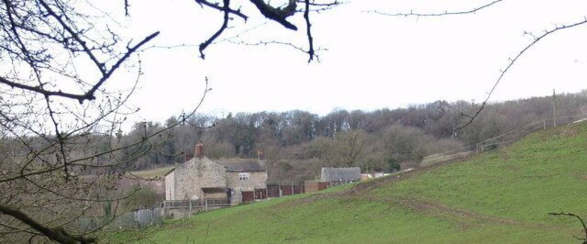 A rural landscape with a grassy hill, a stone building, and trees in the background.