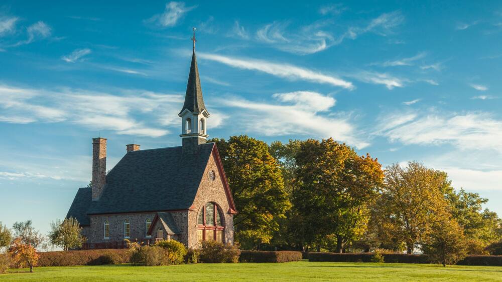 Une église dotée d’un clocher, entourée d’une pelouse verdoyante et d’arbres.