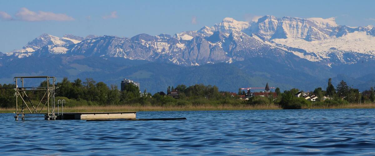A calm lake with a dock and a mountain range in the background.