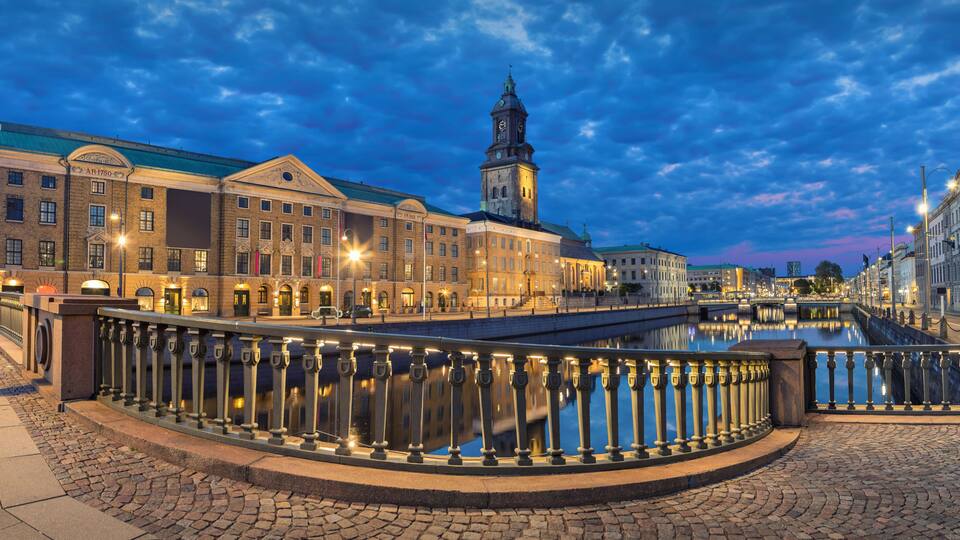 A historic European town square with a prominent clock tower, cobblestone streets, and a bridge over a canal.