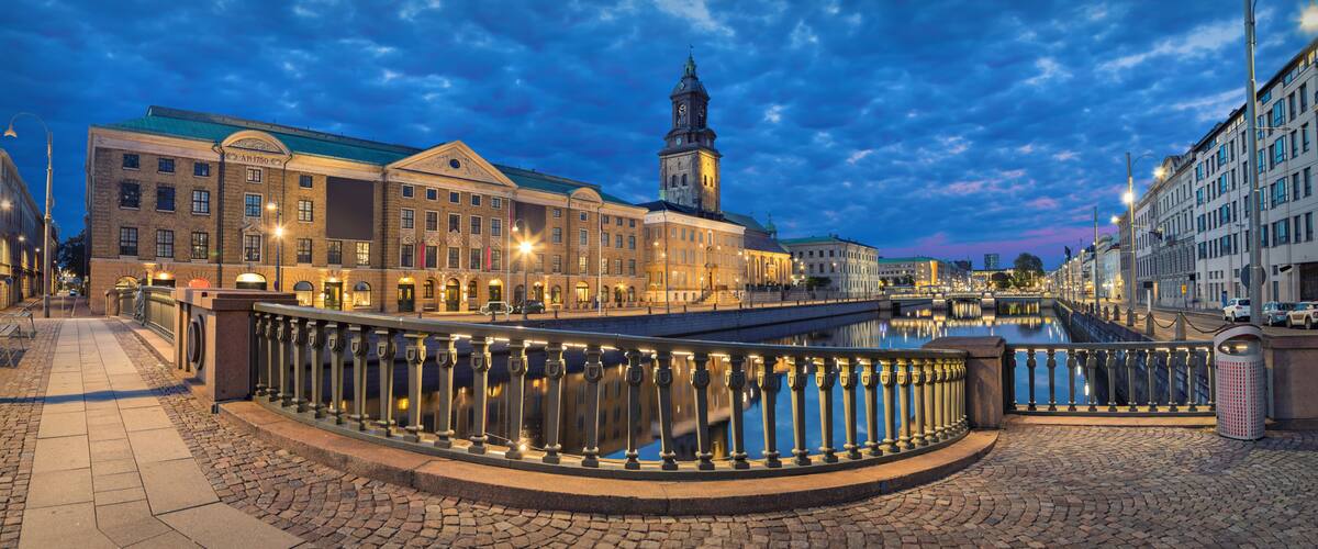 A historic European town square with a prominent clock tower, cobblestone streets, and a bridge over a canal.