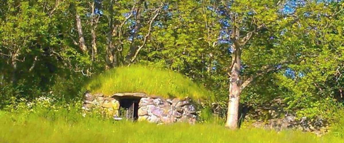 A stone structure in a grassy field with trees in the background.