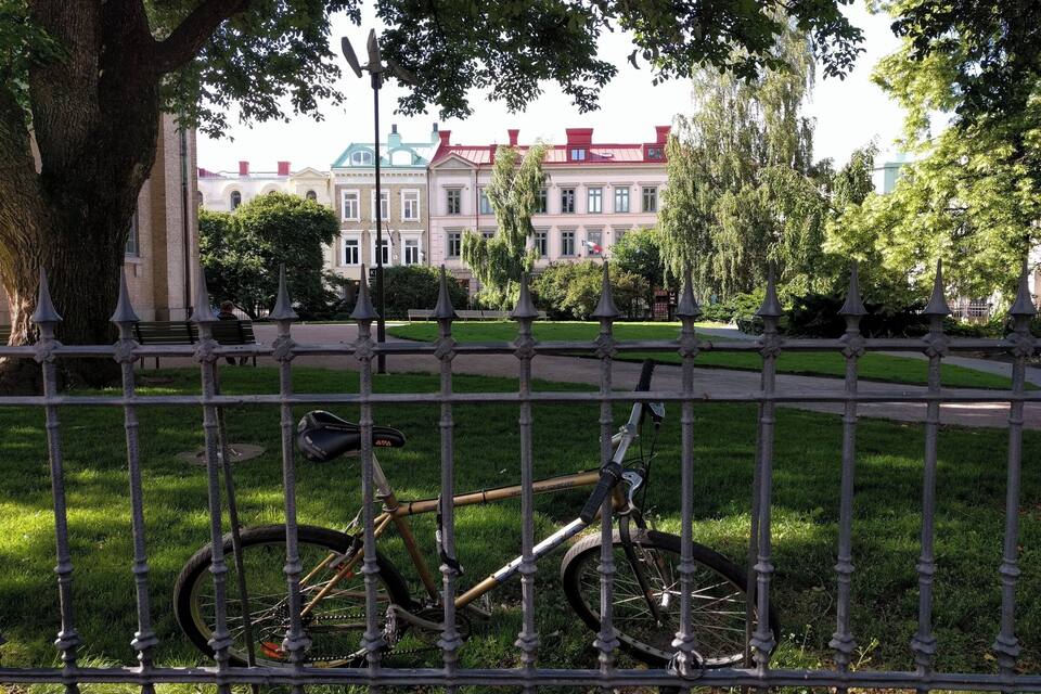 Un vélo appuyé contre une clôture dans un parc, avec un bâtiment en arrière-plan.