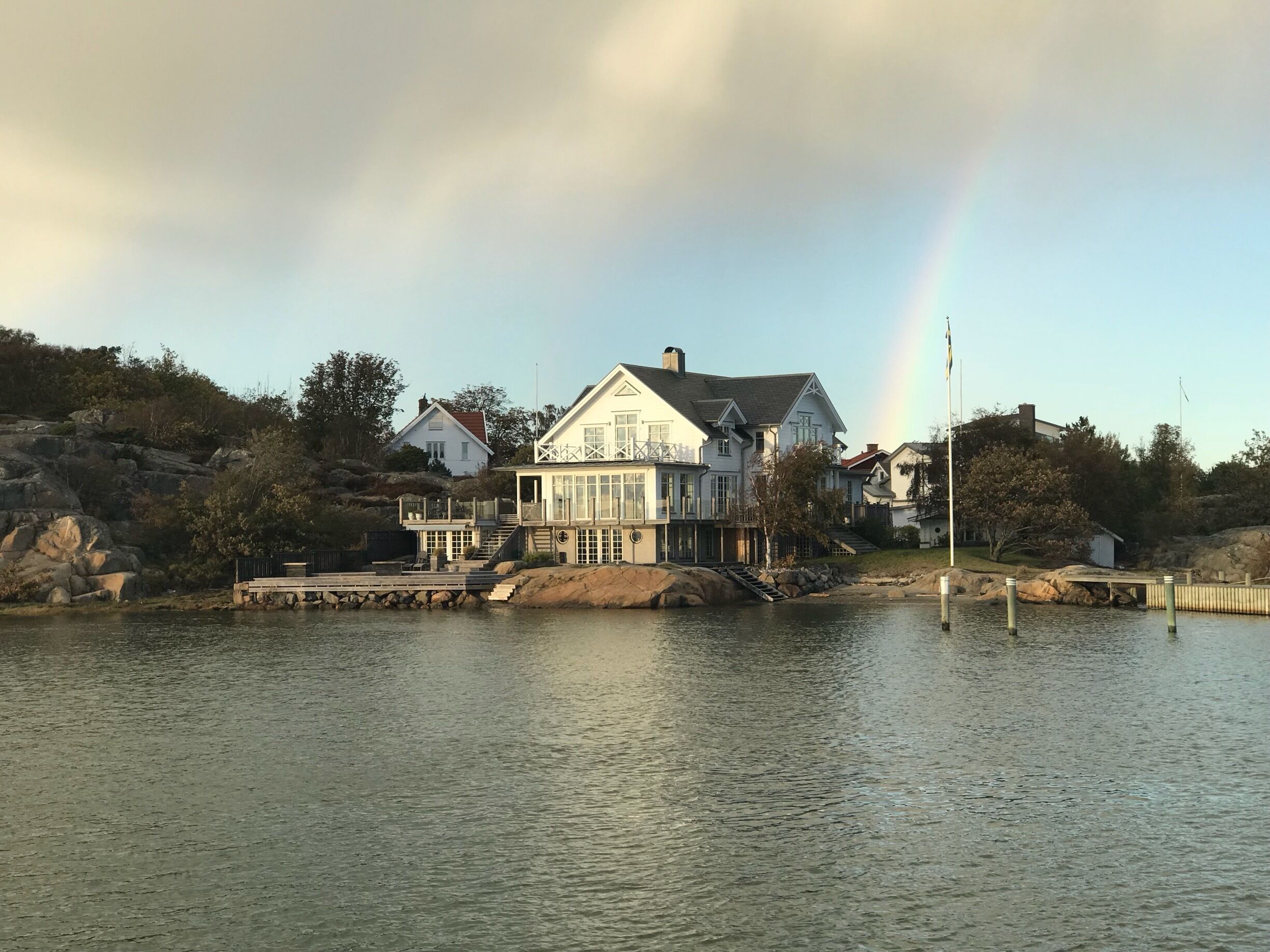 A waterfront house with a dock and a rainbow in the background.