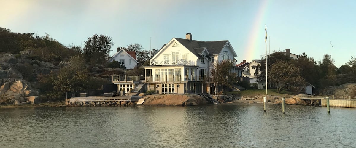 A waterfront house with a dock and a rainbow in the background.
