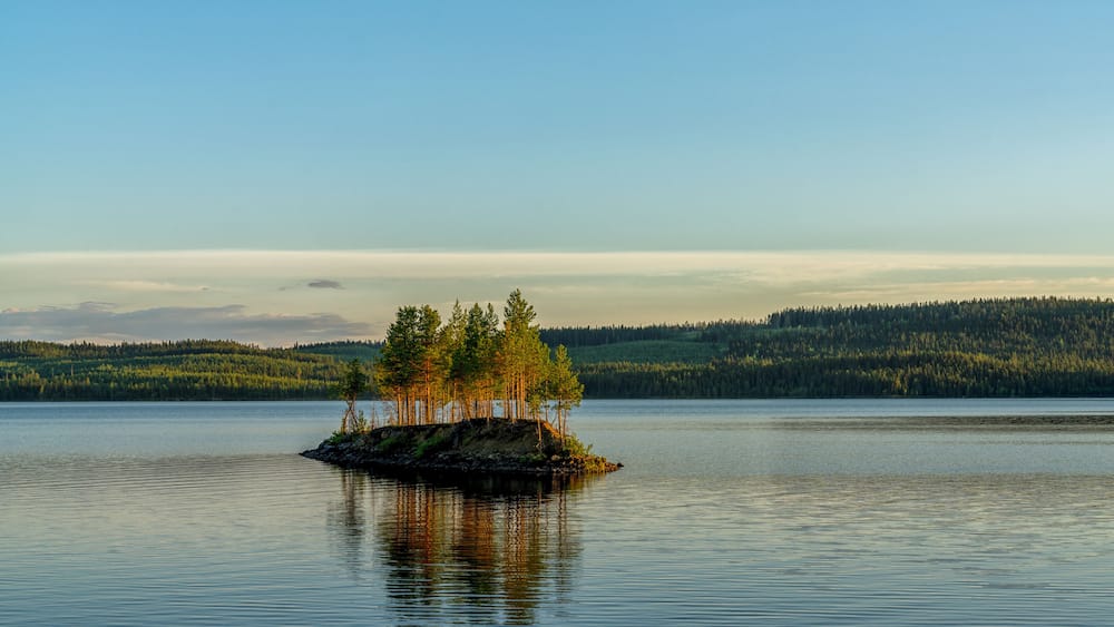idyllic lake landscape with a small island with trees under a cloudless blue sky