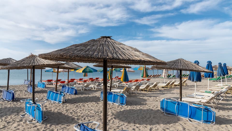 A beach with sun umbrellas, lounge chairs, and a sandy shore.