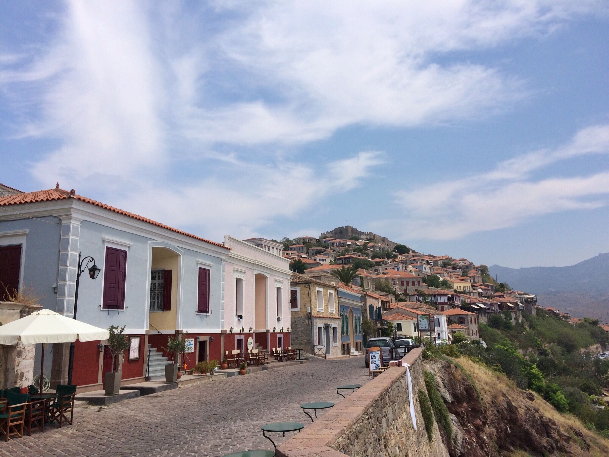A cobblestone street lined with colorful buildings, a stone wall, and a hill with a castle in the background.
