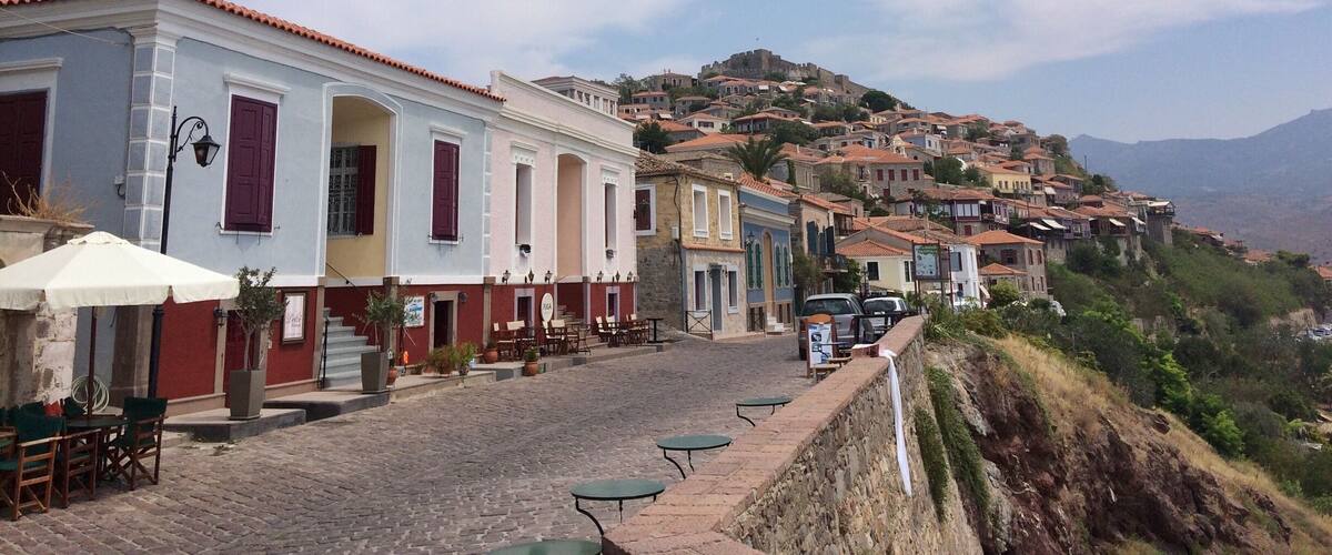A cobblestone street lined with colorful buildings, a stone wall, and a hill with a castle in the background.