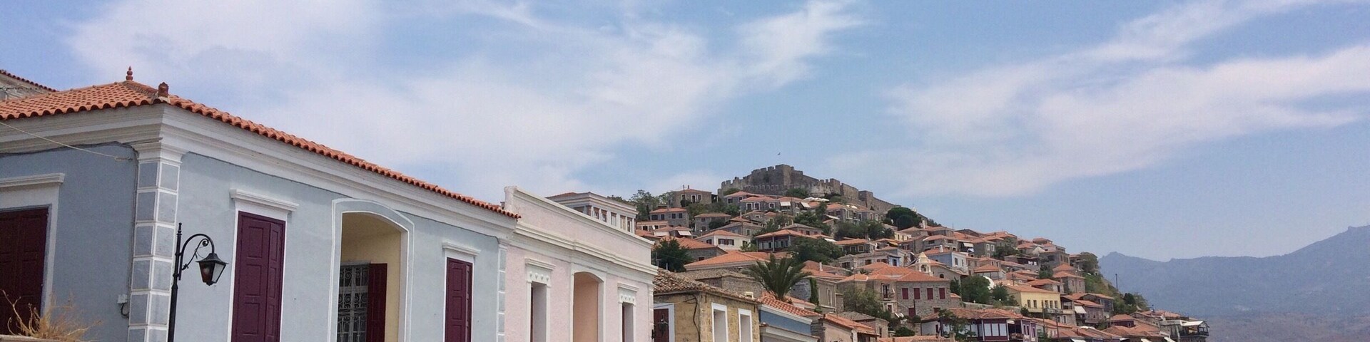 A cobblestone street lined with colorful buildings, a stone wall, and a hill with a castle in the background.