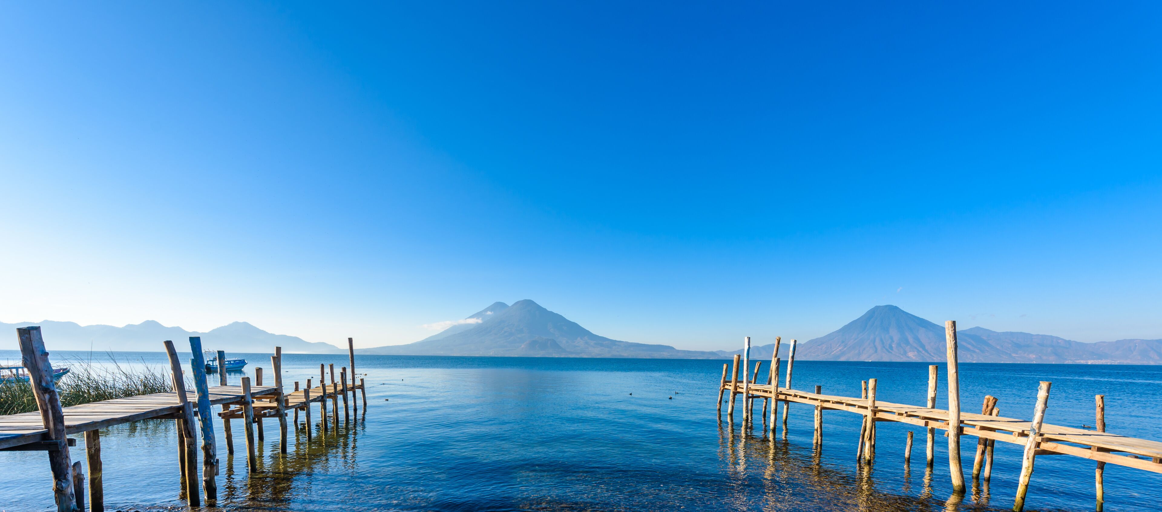 A wooden pier extending into calm waters with mountains in the background.