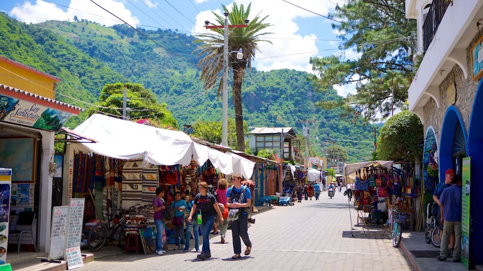 A bustling street market with colorful stalls, a palm tree, and a mountainous backdrop.