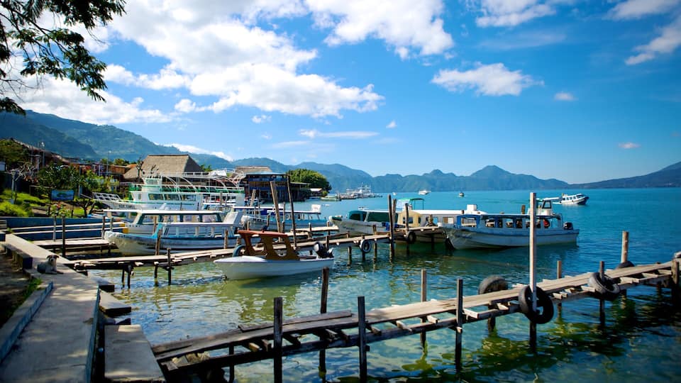 A harbor with boats docked, a wooden pier, and mountains in the background.