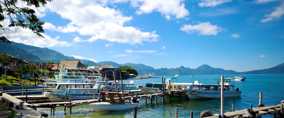 A harbor with boats docked, a wooden pier, and mountains in the background.