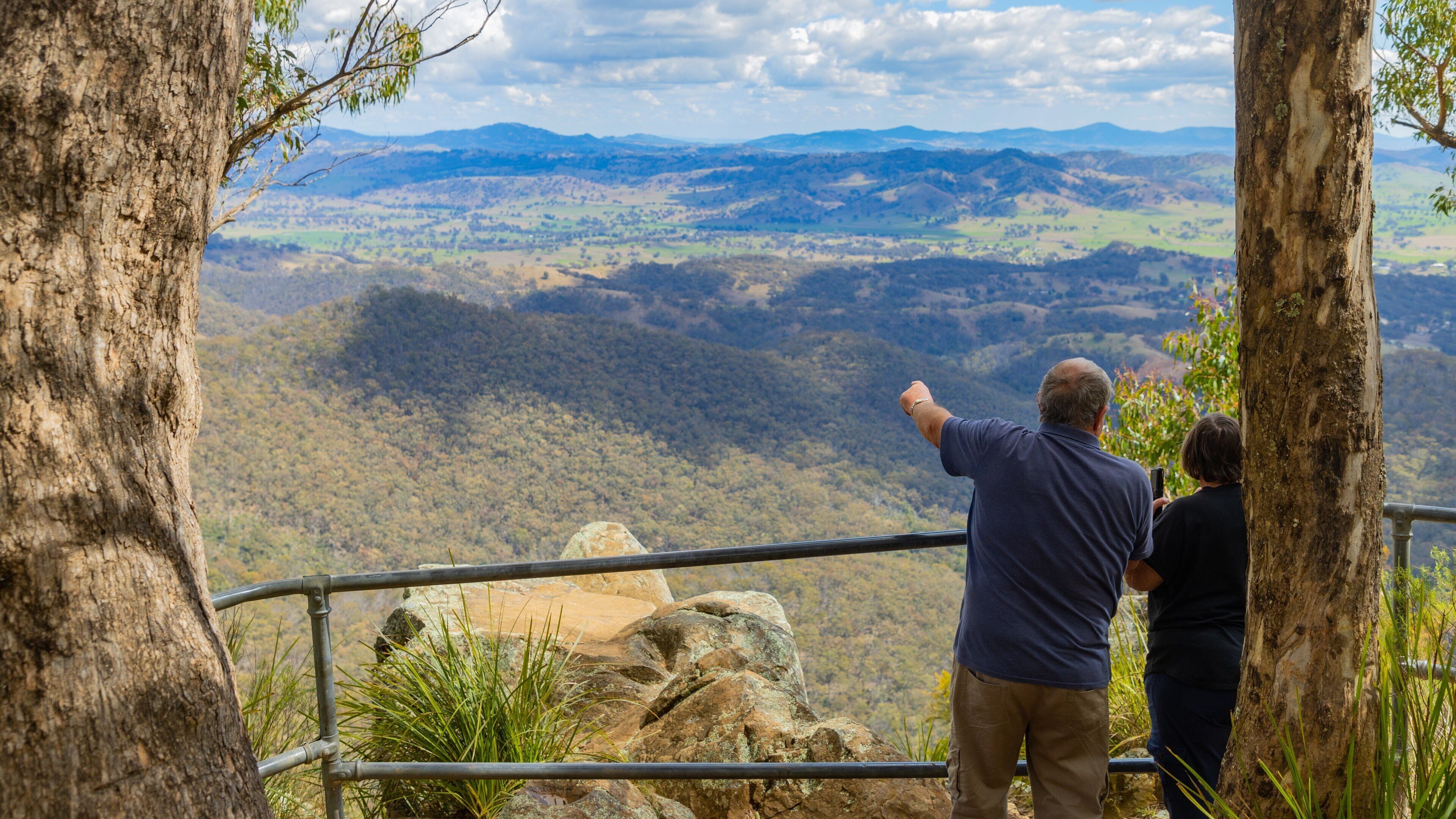 Una pareja contempla un paisaje montañoso con barandilla.