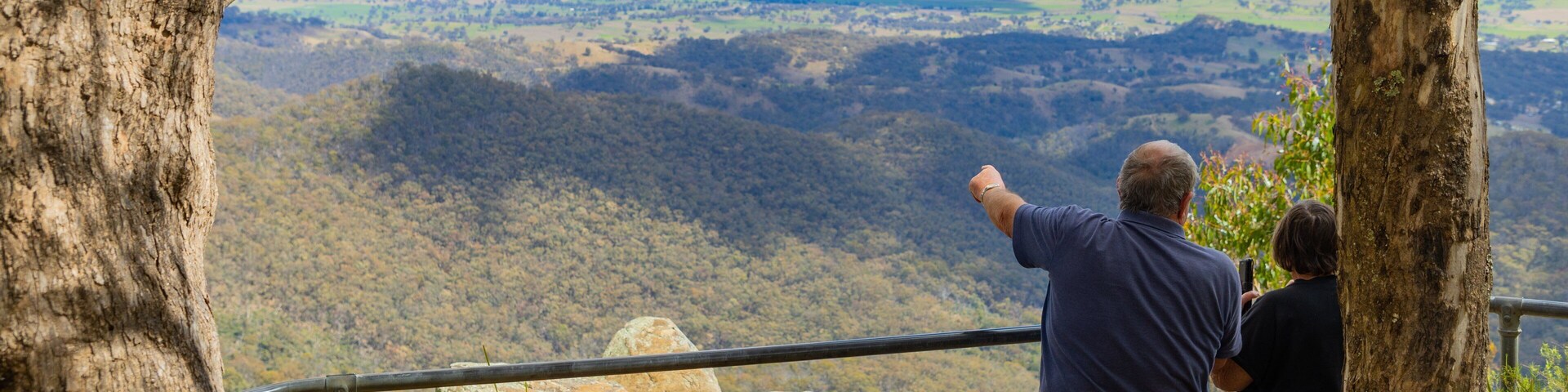 Una pareja contempla un paisaje montañoso con barandilla.
