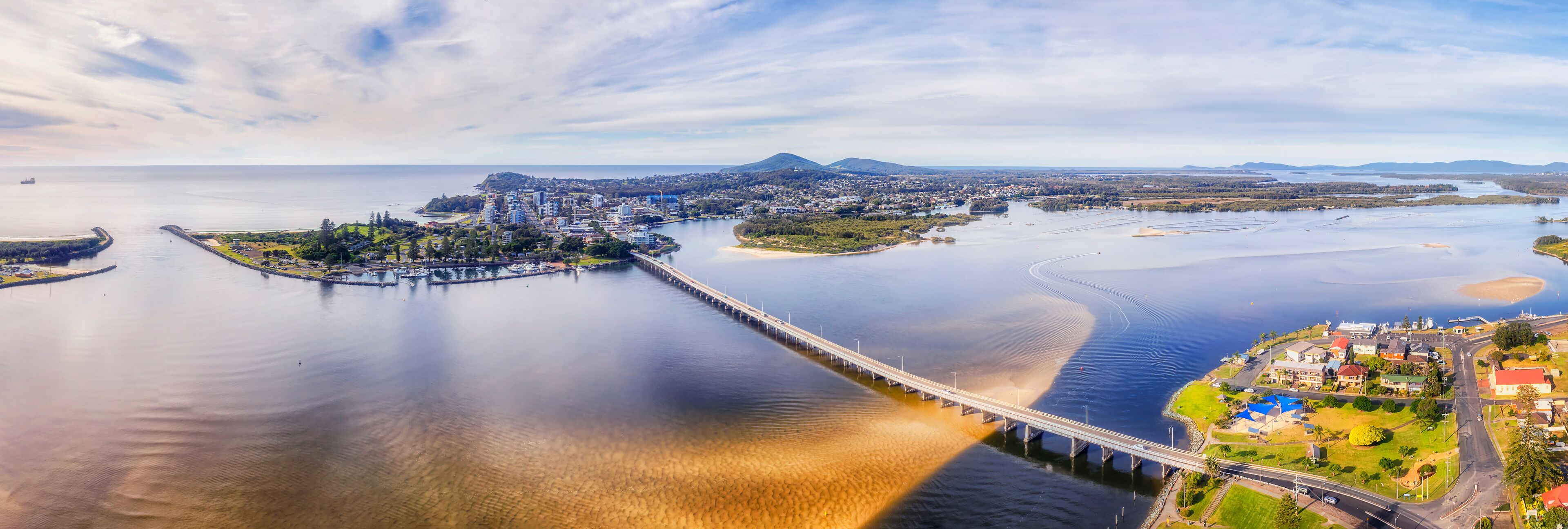 A coastal city with a bridge connecting two landmasses, a large body of water, and distant mountains.