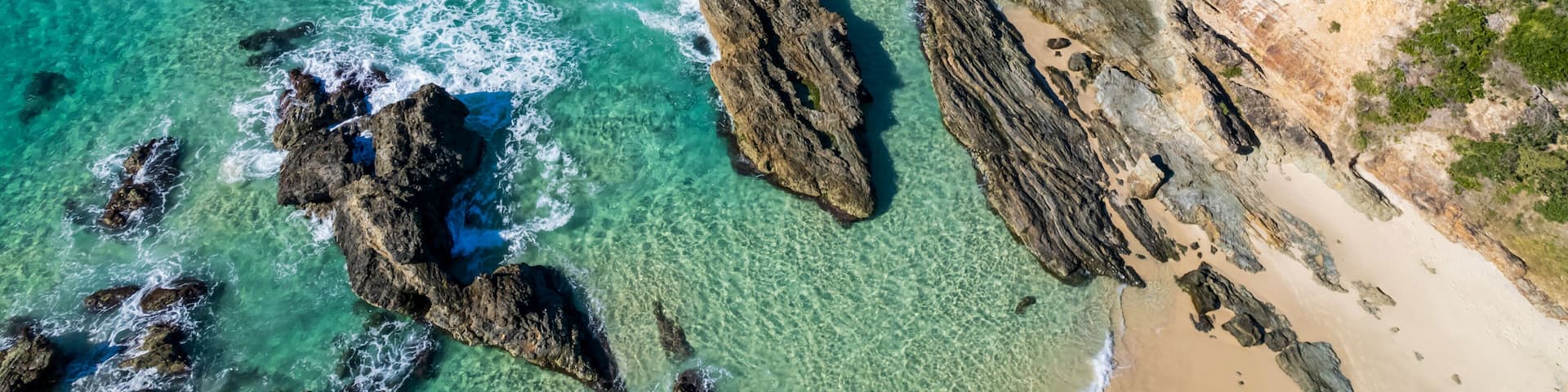 A coastal landscape with clear turquoise waters, rocky outcrops, and a sandy beach.