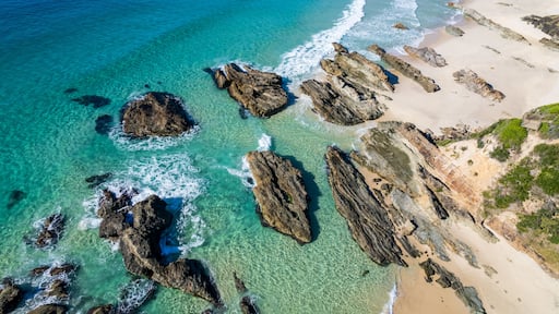 A coastal landscape with clear turquoise waters, rocky outcrops, and a sandy beach.