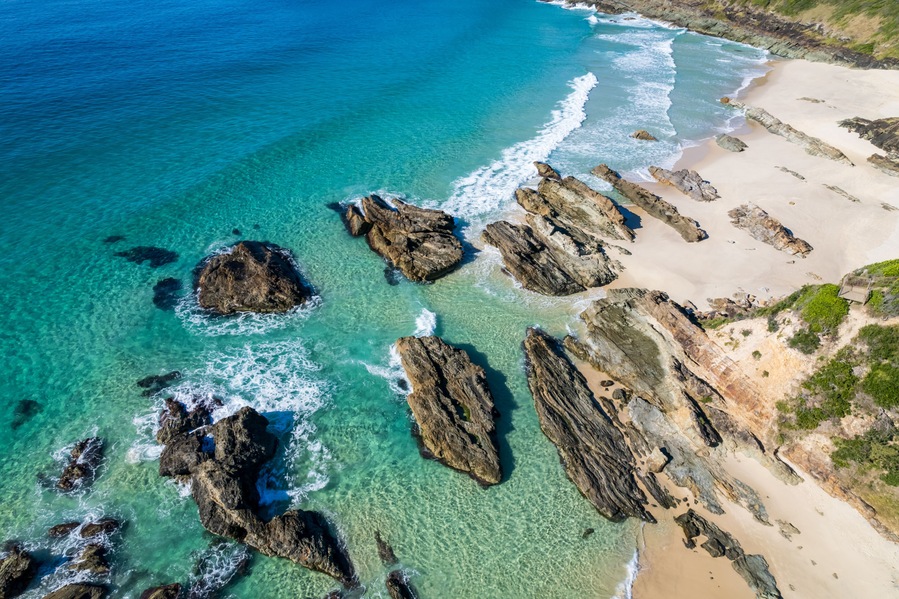 A coastal landscape with clear turquoise waters, rocky outcrops, and a sandy beach.