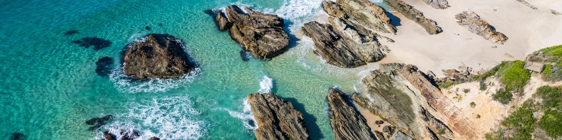 A coastal landscape with clear turquoise waters, rocky outcrops, and a sandy beach.