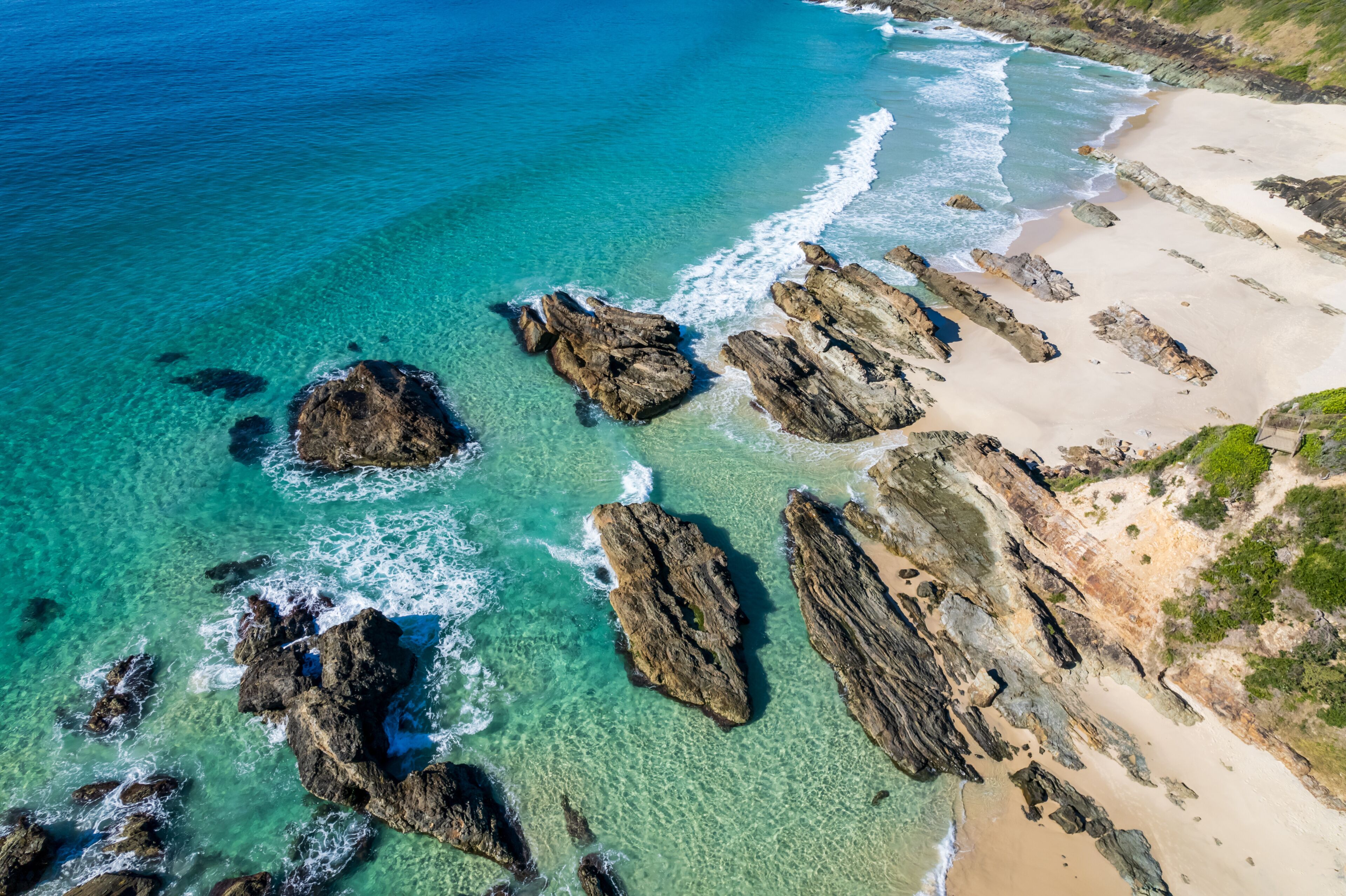 A coastal landscape with clear turquoise waters, rocky outcrops, and a sandy beach.