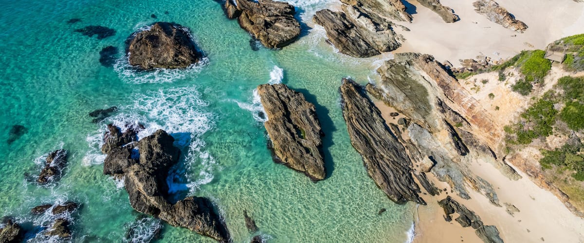 A coastal landscape with clear turquoise waters, rocky outcrops, and a sandy beach.