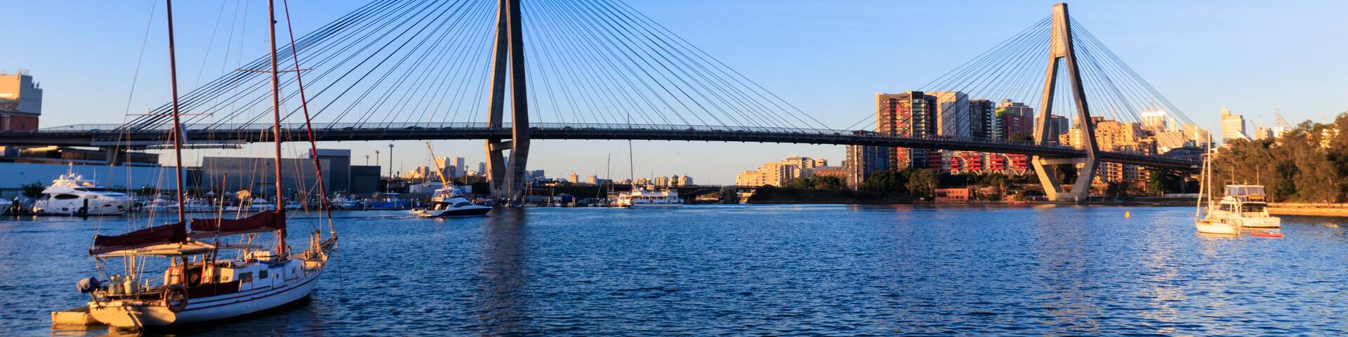 A cable-stayed bridge spanning a river with boats and city buildings in the background.