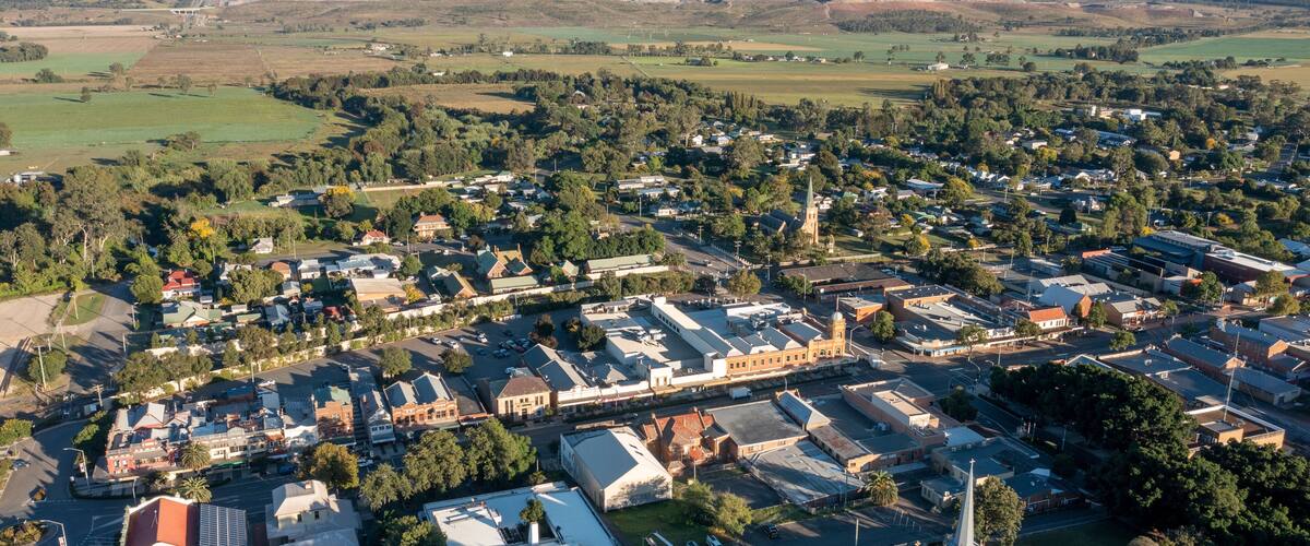 An aerial view of a town with a prominent church, a mix of residential and commercial buildings, and surrounding green fields.