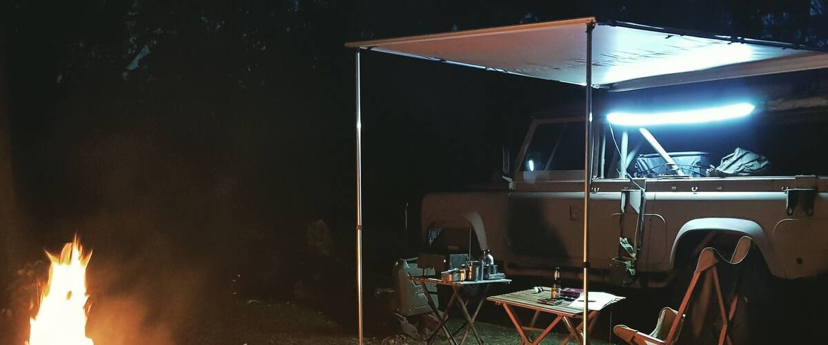 A campfire, a tent, and a vehicle in a nighttime outdoor setting.