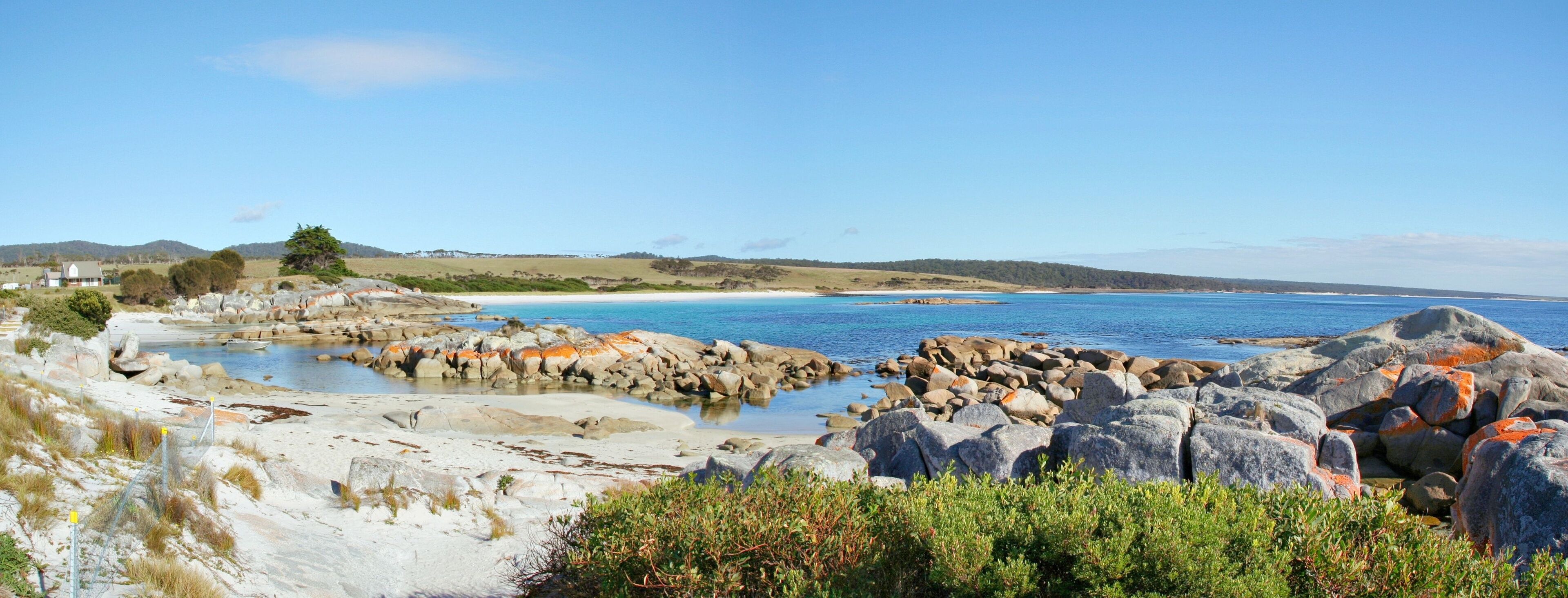A coastal landscape with rocky shores, a sandy beach, and a clear blue sea.