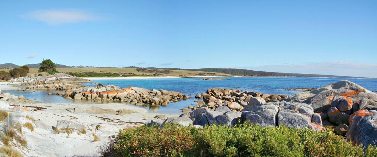 A coastal landscape with rocky shores, a sandy beach, and a clear blue sea.
