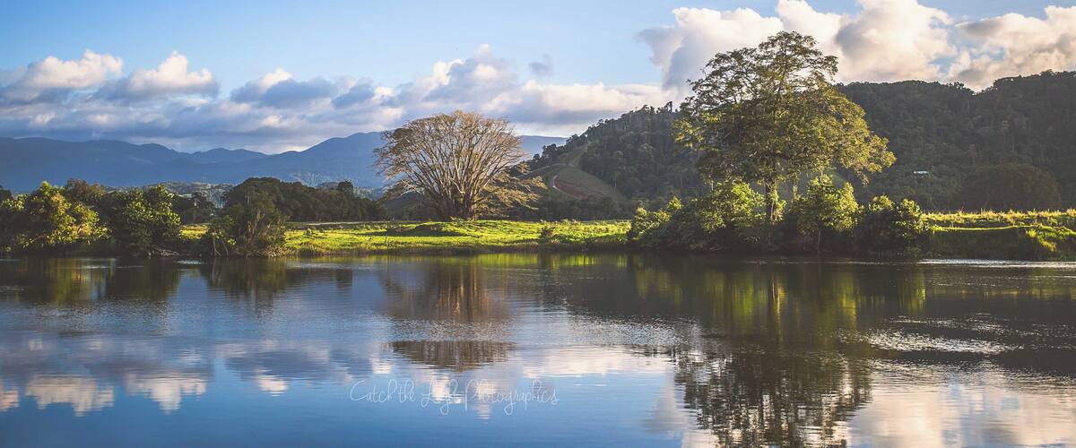 A calm lake with reflections of trees and mountains in the background.