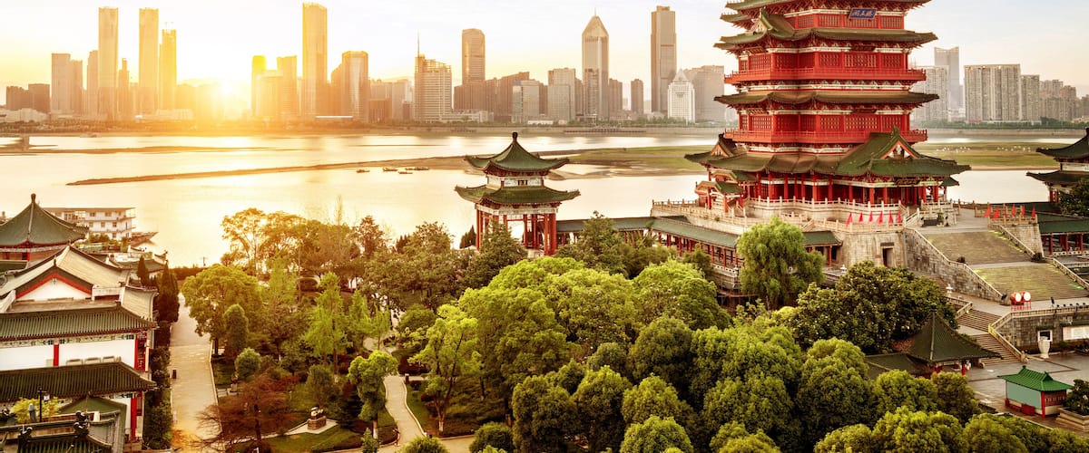 A traditional pagoda with multiple tiers, a river, and a modern city skyline in the background.