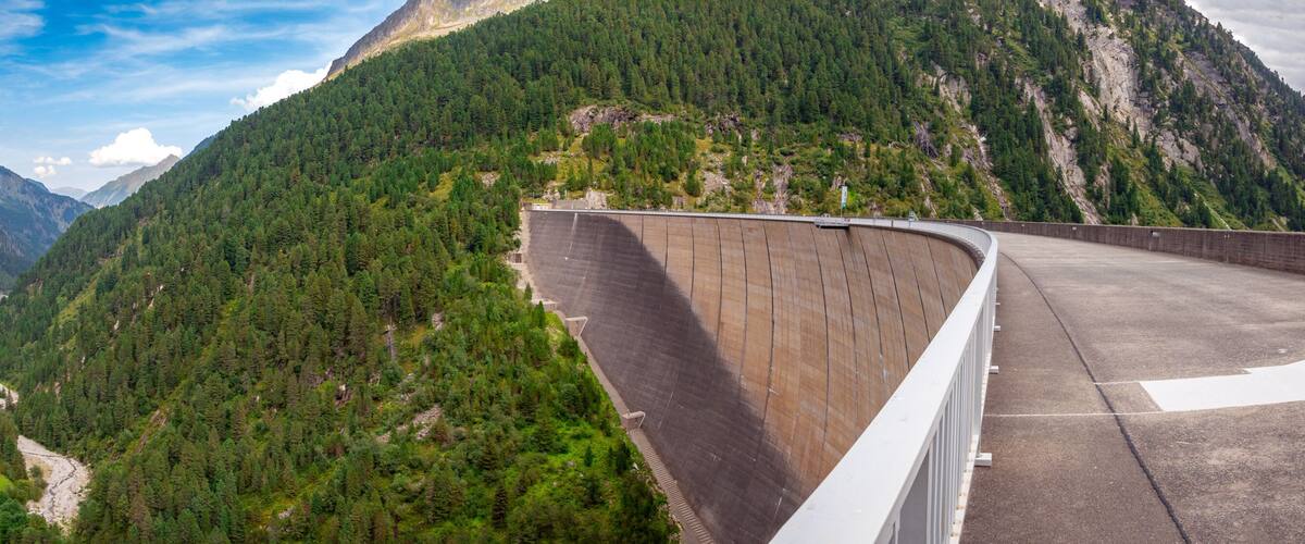 A dam, a winding road, and a valley with dense forests and mountains.