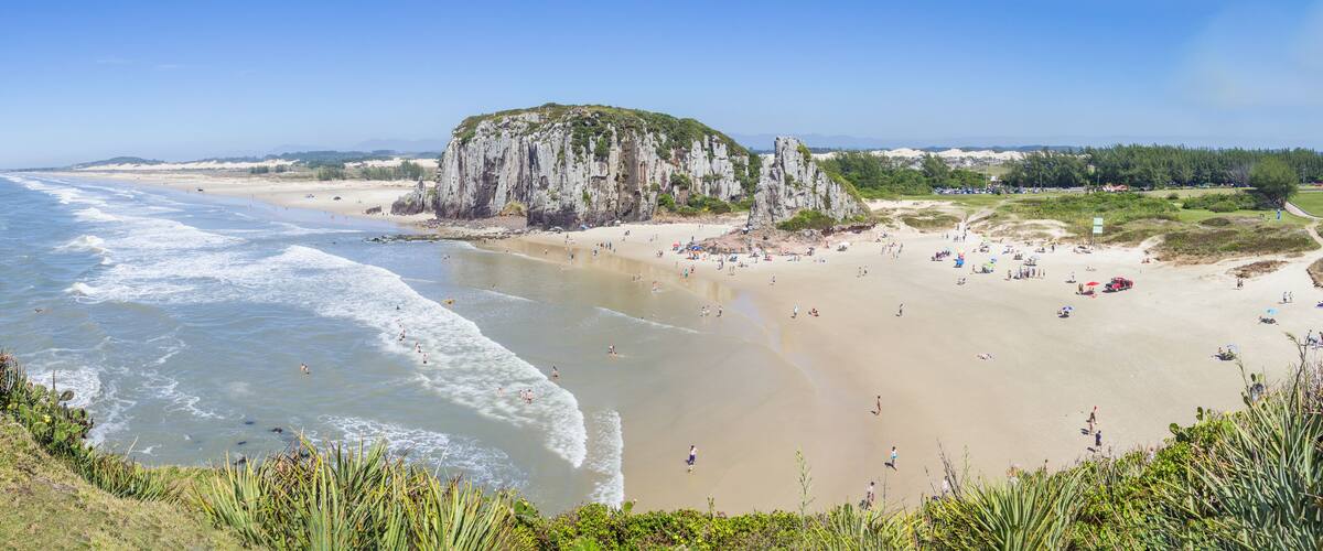 A coastal beach with waves, a sandy shore, and a rocky cliff.