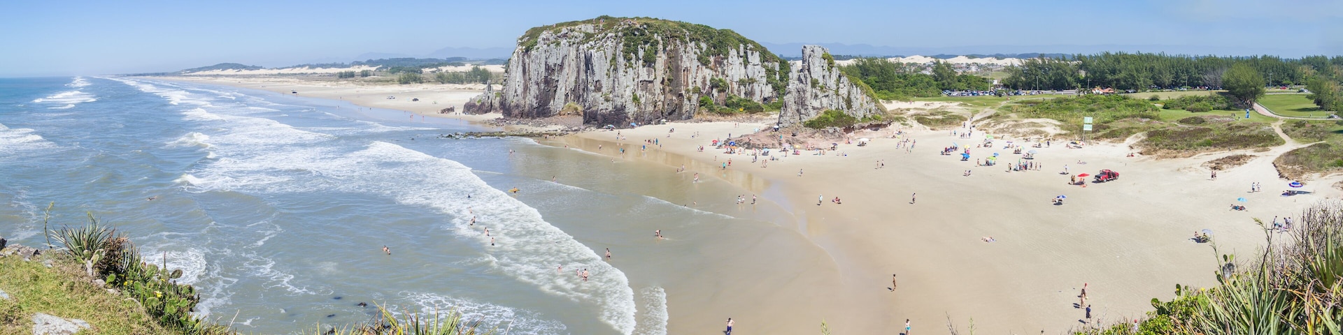 A coastal beach with waves, a sandy shore, and a rocky cliff.